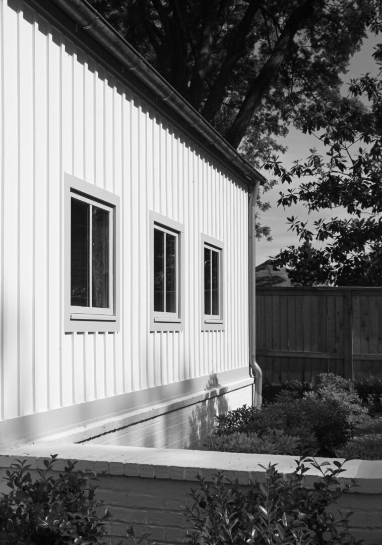 A black and white photo of three windows on the side of a building.