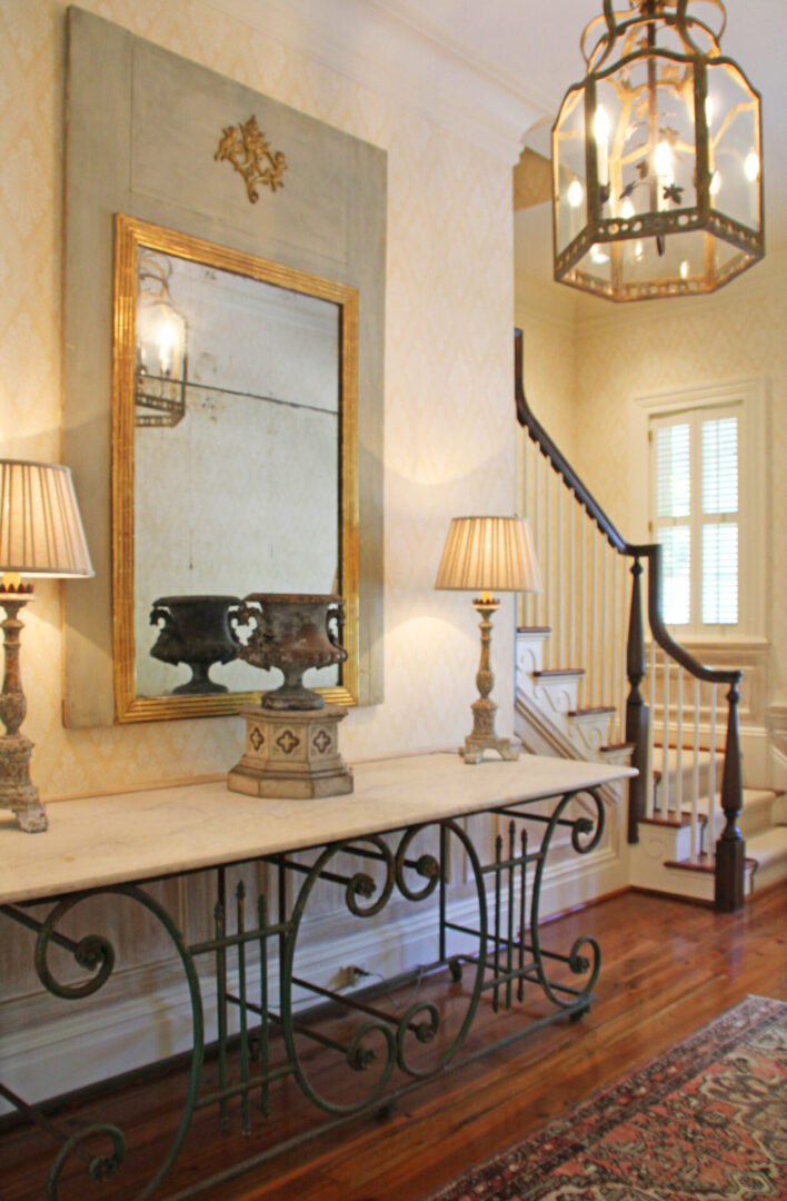 A foyer with a table and lamps, mirror and staircase.