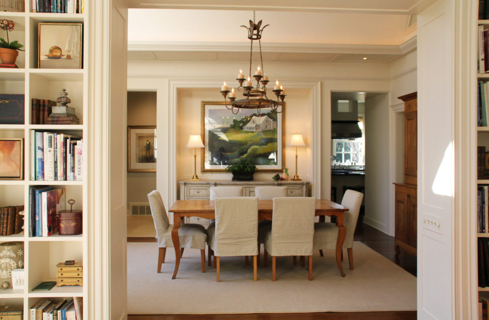 A dining room with a table and chairs, lamps and pictures on the wall.