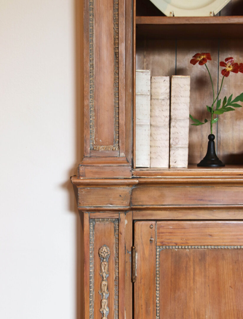 A wooden cabinet with books and flowers on top of it.