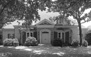 A black and white photo of a house with trees in the background.