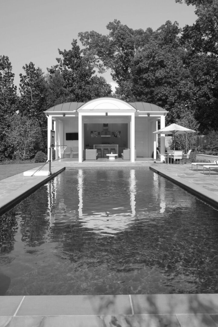 A pool with an umbrella and chairs in the background.