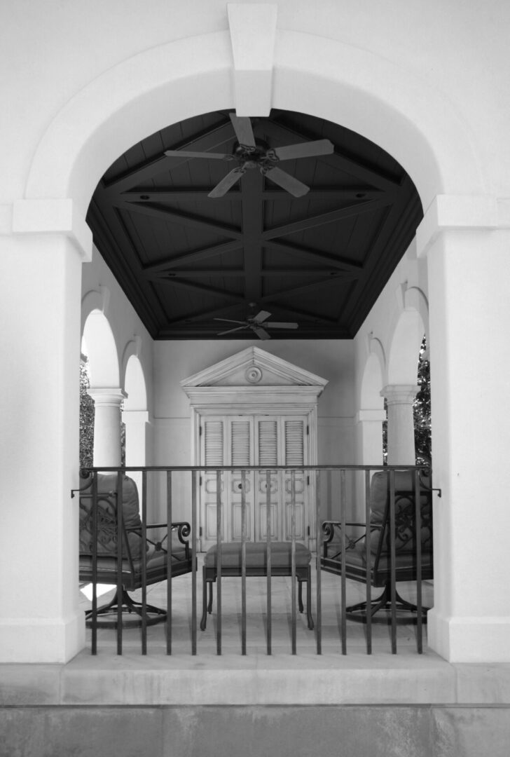 A black and white photo of two chairs in front of an archway.