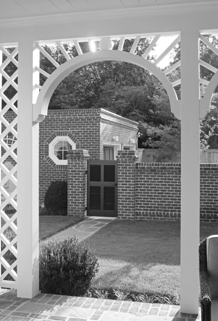 A black and white photo of an archway in the middle of a garden.