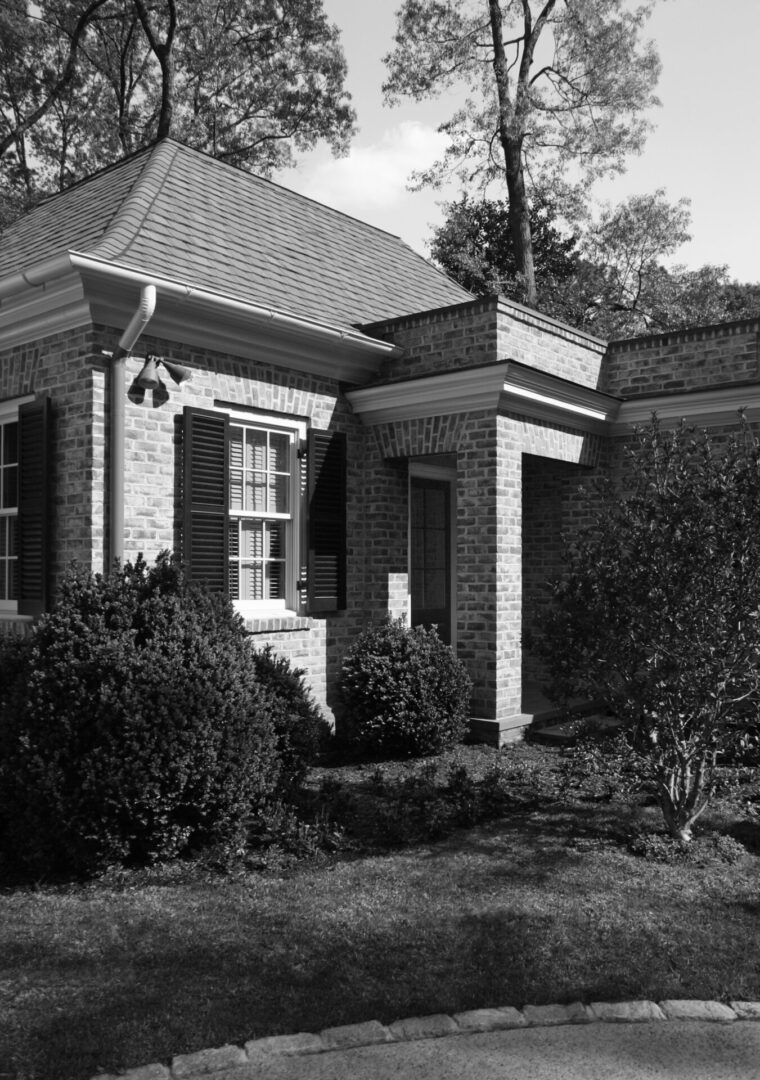 A black and white photo of a house with bushes around it.