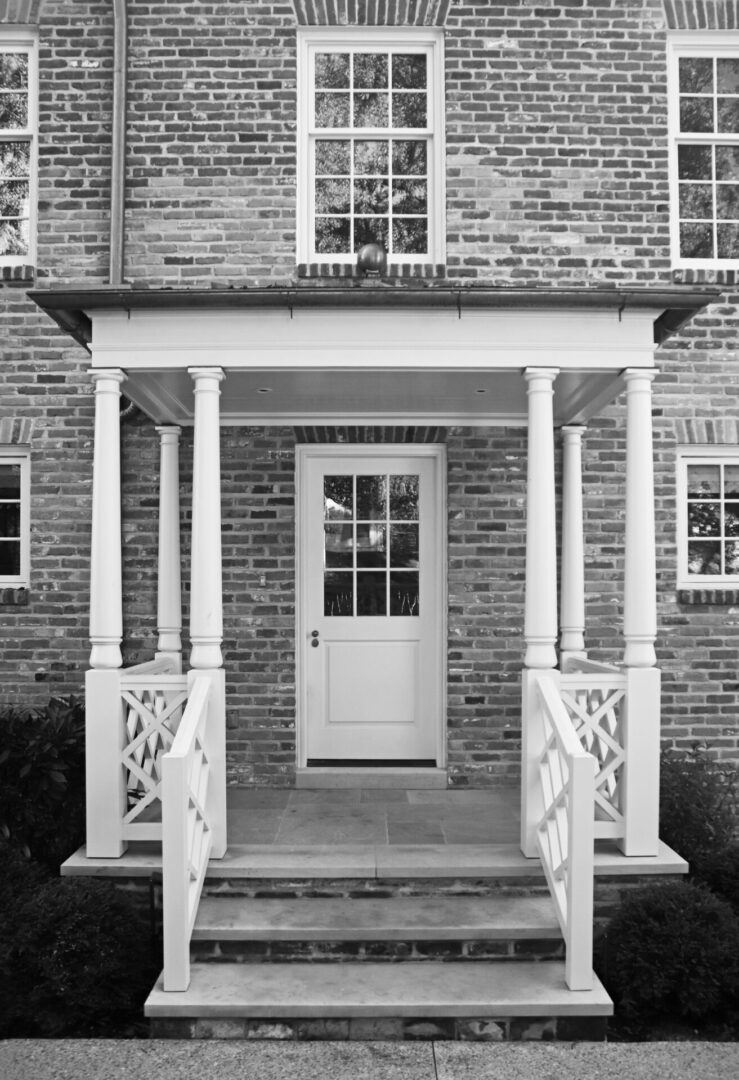 A black and white photo of a American Georgian porch with steps leading to the front door.