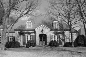A black and white photo of a house with trees in front.