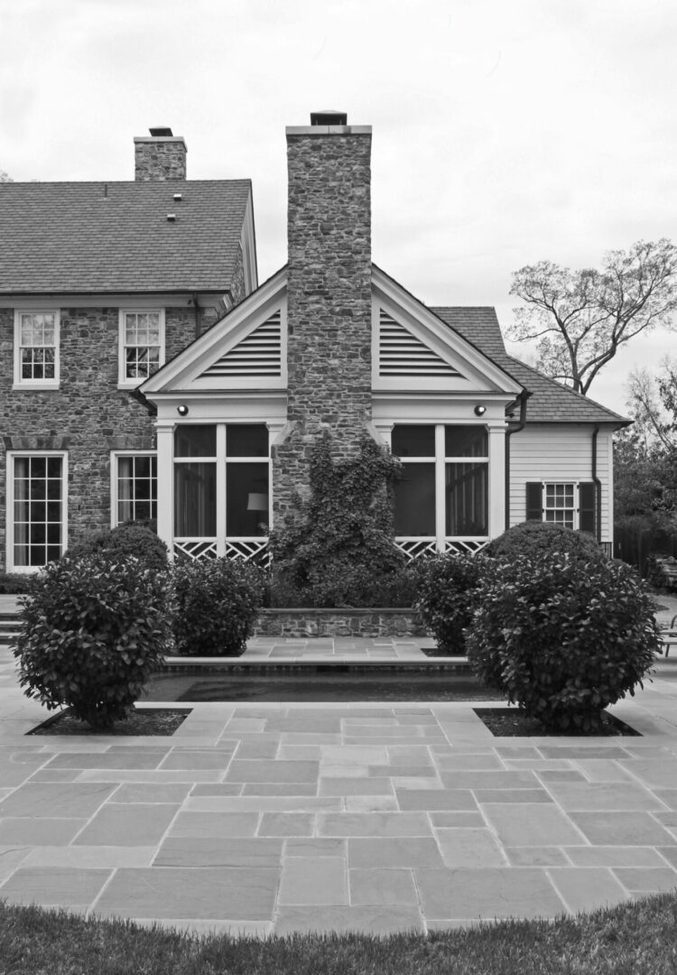 A black and white photo of a house with bushes in front.