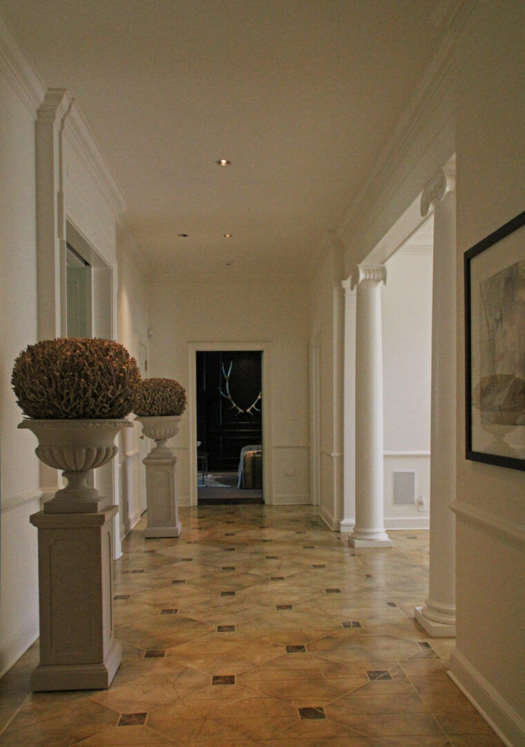 A hallway with pillars and a vase on the floor.